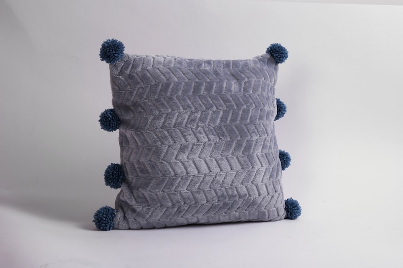 May include: A gray throw pillow with a textured chevron pattern and blue pom-poms around the edges.