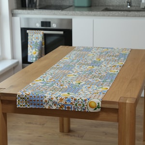 May include: A white table runner with a blue and yellow lemon pattern. The runner is on a wooden table with a white background.