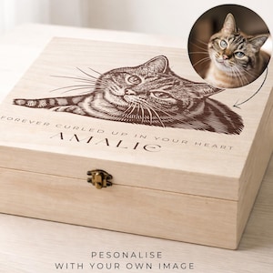 以下が含まれることがあります： 明るい色の木製ボックスで、蓋には猫の詳細な彫刻画像があります。 蓋には「FOREVER CURLED UP IN YOUR HEART」というテキストと名前も表示されています。 彫刻された画像の隣には、猫の円形画像があります。 ボックスには金属製の留め金が付いています。