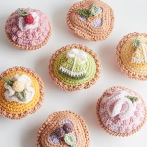 May include: Six crocheted mini pies with various fillings, including a green lime pie, a pink strawberry pie, and a yellow lemon pie. The pies are all heart-shaped or round and have a brown crust.