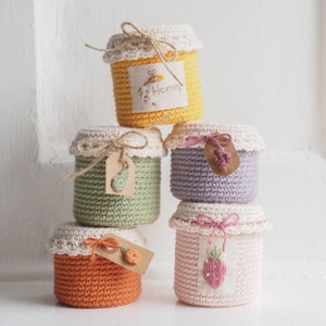 May include: Five crocheted jars with labels and decorative details. The jars are stacked on top of each other. The top jar is yellow and says "Honey". The next jar is purple, the next is green, the next is orange, and the bottom jar is pink.