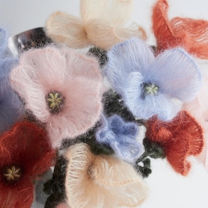 May include: A collection of handmade, fluffy flowers in various pastel colors, including pink, blue, peach, and red. The flowers have a delicate, textured appearance and are clustered together, possibly for a decorative arrangement or craft project.