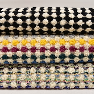 May include: Four different types of textured fabric with various colors and patterns. The top fabric is black and white, the second is gray, yellow, burgundy, and green, the third is blue, green, and white, and the bottom is a multi-colored fabric with a white background.
