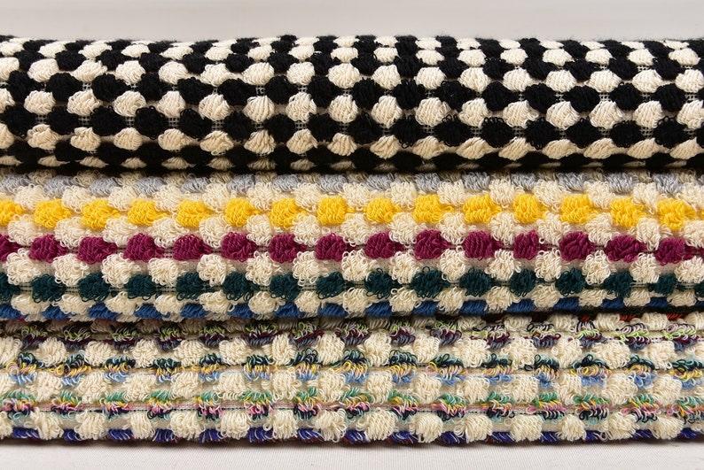 May include: Four different types of textured fabric with various colors and patterns. The top fabric is black and white, the second is gray, yellow, burgundy, and green, the third is blue, green, and white, and the bottom is a multi-colored fabric with a white background.