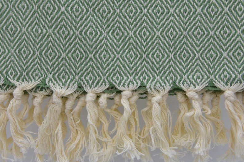 May include: A green and white patterned Turkish towel with a fringe border. The towel is made of cotton and has a soft, absorbent texture.