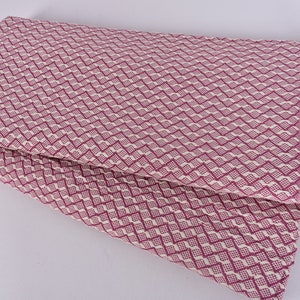 May include: A pink and white patterned throw blanket with fringe. The blanket is folded in half and has a diamond pattern.