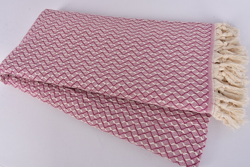 May include: A pink and white patterned throw blanket with fringe. The blanket is folded in half and has a diamond pattern.