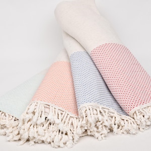 Puede incluir: Cuatro toallas turcas enrolladas en colores pastel: verde claro, rosa, azul y rojo. Cada toalla tiene un fleco blanco y un patrón tejido en la sección coloreada. Las toallas están hechas de material suave y absorbente.