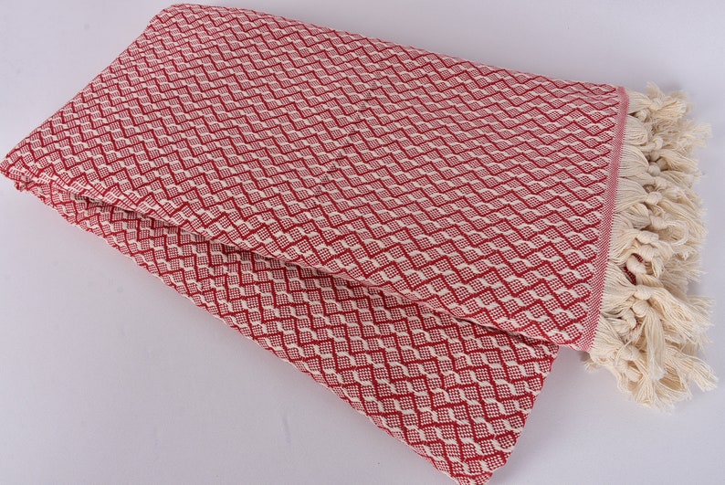 May include: Red and white patterned throw blanket with fringe. The blanket is folded in half and has a diamond pattern.