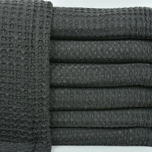 Peut inclure: Une pile de serviettes en tissu gaufré gris foncé avec des bords frangés.