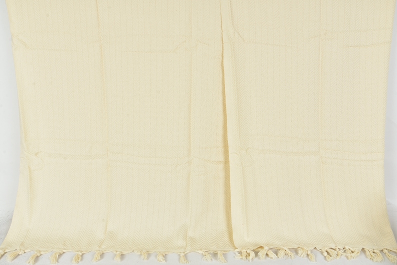 May include: A cream-colored throw blanket with a woven texture and fringe trim.