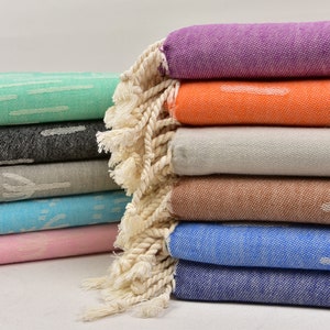 May include: A stack of colourful towels with fringed edges. The towels are folded and arranged in a pyramid shape. The towels are in various colours, including purple, orange, white, brown, blue, and pink.