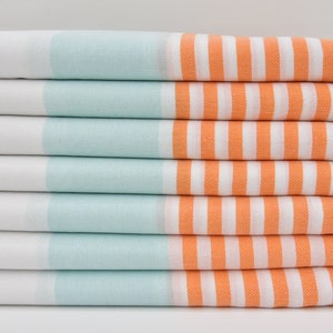 Könnte beinhalten: Ein Stapel von sechs gestreiften Handtüchern in Weiß, Hellblau und Orange. Die Handtücher haben an den Enden Fransen.