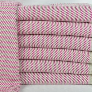 May include: A stack of pink and beige striped towels with white fringe. The towels are folded and stacked on a white surface.