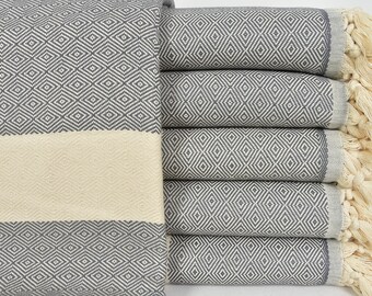 May include: A stack of grey and white patterned Turkish towels with fringe. The towels are folded and stacked on a white surface.