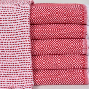 May include: A stack of red and white Turkish towels with a diamond pattern. The towels have white fringe on the ends.