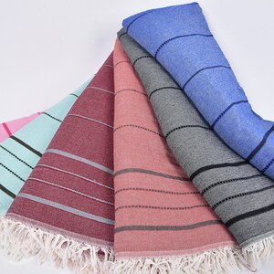 May include: Five striped beach towels in different colors, including pink, light blue, burgundy, coral, and gray. The towels have white fringe around the edges.