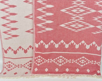 Puede incluir: Dos toallas turcas de color rosa y blanco con flecos en los bordes. Las toallas tienen un diseño geométrico con diamantes y triángulos blancos sobre un fondo rosa.