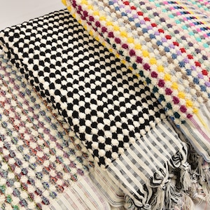 May include: Three Turkish towels with different patterns. The first towel is white with a multi-colored dot pattern. The second towel is black and white with a checkered pattern. The third towel is white with a black and white checkered pattern.