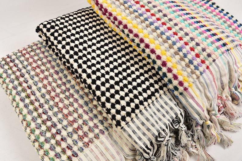 May include: Three Turkish towels with different patterns. The first towel is white with a multi-colored dot pattern. The second towel is black and white with a checkered pattern. The third towel is white with a black and white checkered pattern.