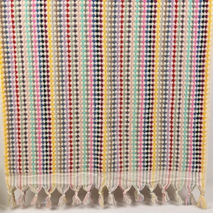 May include: A colorful striped hand towel with a fringe border. The towel is made of a soft, absorbent material and features a variety of colors, including pink, blue, green, yellow, and red.