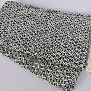 May include: A green and white patterned throw blanket with a fringe border. The blanket is folded in half and has a diamond pattern.