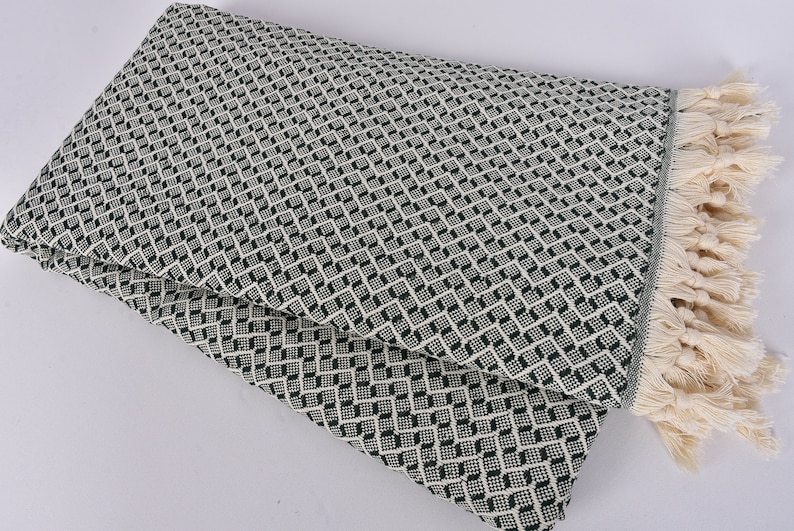 May include: A green and white patterned throw blanket with a fringe border. The blanket is folded in half and has a diamond pattern.