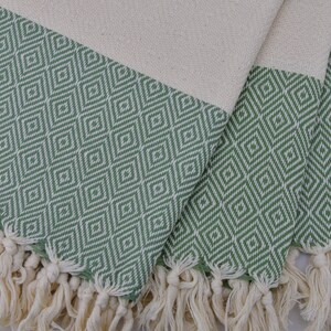 May include: A green and white patterned Turkish towel with fringe. The towel is folded in thirds and the fringe is visible on all three sides.
