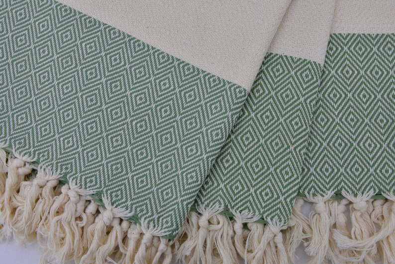 May include: A green and white patterned Turkish towel with fringe. The towel is folded in thirds and the fringe is visible on all three sides.