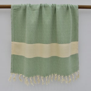 May include: A green and white patterned Turkish towel with fringe. The towel has a white stripe in the middle.