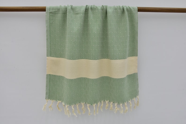 May include: A green and white patterned Turkish towel with fringe. The towel has a white stripe in the middle.