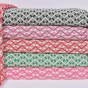 May include: A stack of five patterned throw blankets with fringe. The blankets are in various colours, including red, green, pink, and purple. The blankets are made of a soft, woven fabric.