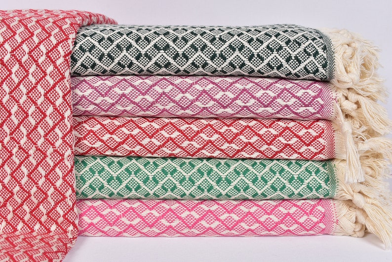 May include: A stack of five patterned throw blankets with fringe. The blankets are in various colours, including red, green, pink, and purple. The blankets are made of a soft, woven fabric.