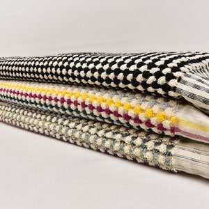 May include: A stack of four towels in different patterns. The top towel is black and white checkered, the second is white with yellow, red, and green stripes, the third is white with blue and green stripes, and the bottom towel is white with a blue and green pattern.