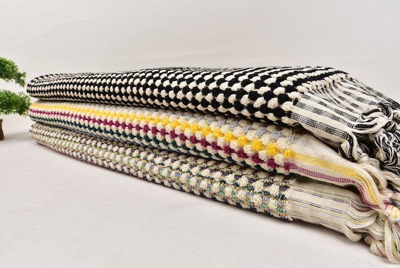 May include: A stack of four towels in different patterns. The top towel is black and white checkered, the second is white with yellow, red, and green stripes, the third is white with blue and green stripes, and the bottom towel is white with a blue and green pattern.