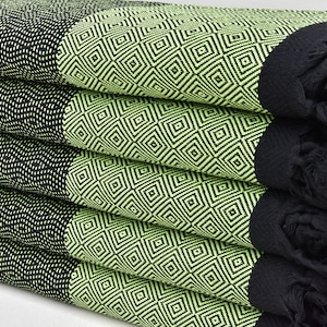 May include: A stack of four green and black patterned towels with black fringe. The towels are folded in half and have a diamond pattern.