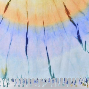 Puede incluir: Una toalla de playa azul y naranja con estampado tie-dye y borde de flecos.