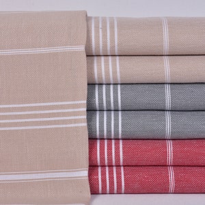 May include: A stack of folded towels in various colors: beige, gray, and red. Each towel features three white stripes near the edge. The towels are made of a textured fabric.