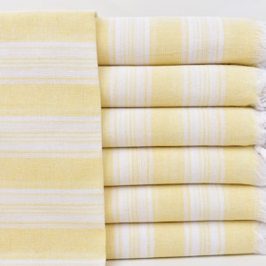 May include: A stack of yellow and white striped towels with fringed edges. The towels are folded and stacked on a white surface.