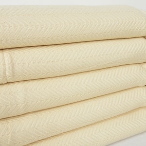 May include: A stack of five cream-colored cotton throw blankets with a herringbone pattern and fringe edges.