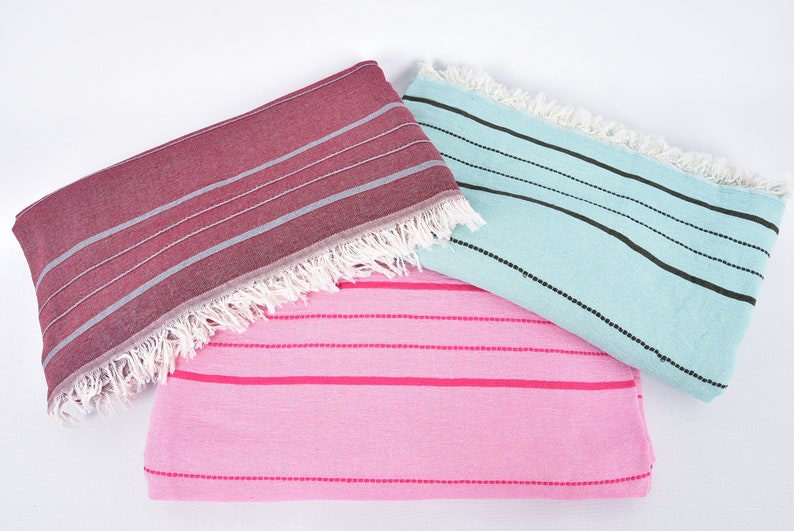 May include: Three striped towels in different colors: pink with hot pink stripes, light blue with black stripes, and burgundy with gray stripes. The towels have white fringe.