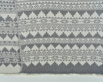 Peut inclure: Une couverture en tissu gris et blanc à motifs avec des franges sur les bords. Le motif est un design géométrique avec des triangles, des carrés et des losanges.