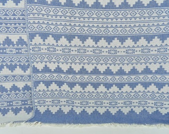 May include: A blue and white patterned throw blanket with fringe on the edges. The pattern is a geometric design with white diamonds and triangles on a blue background.