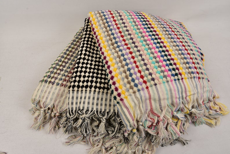 May include: A stack of four Turkish towels with colorful striped and patterned designs. The towels have fringe edges and are made of cotton.
