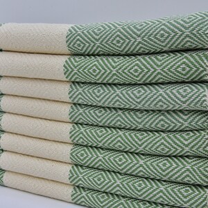 May include: A stack of green and white patterned Turkish towels with fringe. The towels are folded and stacked on top of each other.