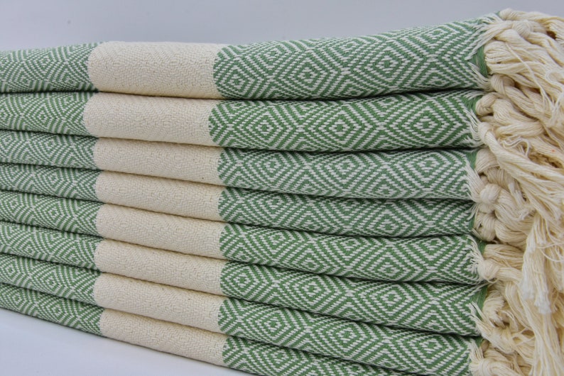 May include: A stack of green and white patterned Turkish towels with fringe. The towels are folded and stacked on top of each other.