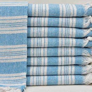 May include: A stack of light blue and white striped towels with white fringe. The towels are folded and stacked on a white surface.