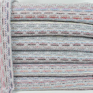 May include: A stack of gray and white striped towels with colorful woven details. The towels have fringe edges and are folded neatly.