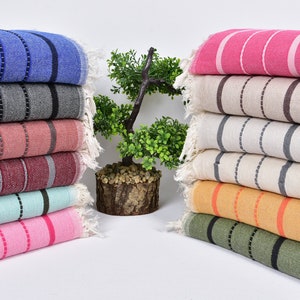 May include: A stack of striped towels in various colors, including blue, gray, pink, red, green, and orange. The towels are folded and arranged in a row on a white surface.