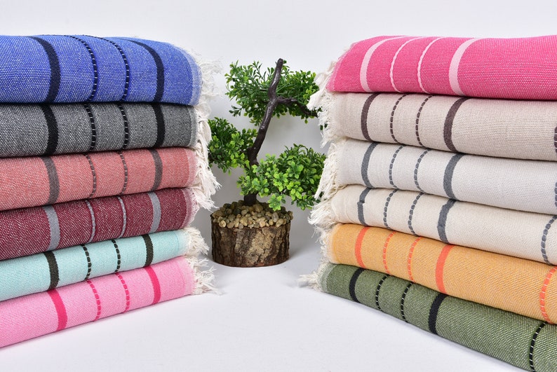 May include: A stack of striped towels in various colors, including blue, gray, pink, red, green, and orange. The towels are folded and arranged in a row on a white surface.